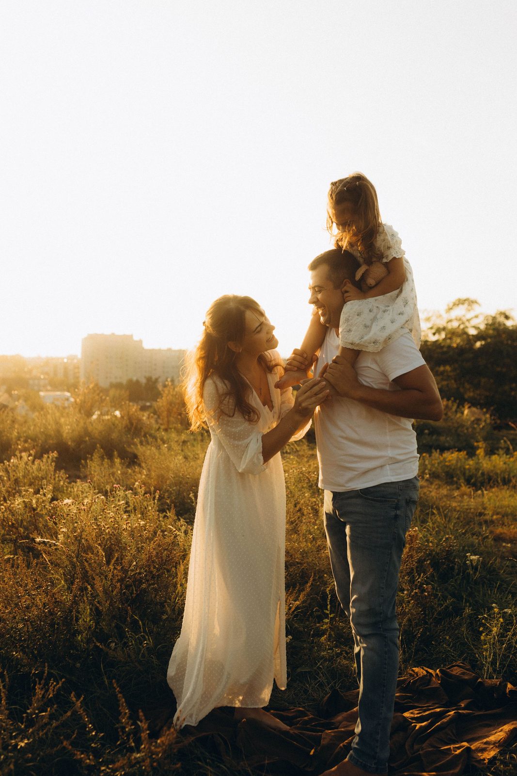 A mother, father and small child together in a field at sunset.